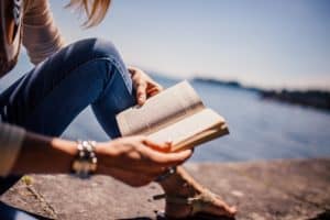 girl reading a book by the water