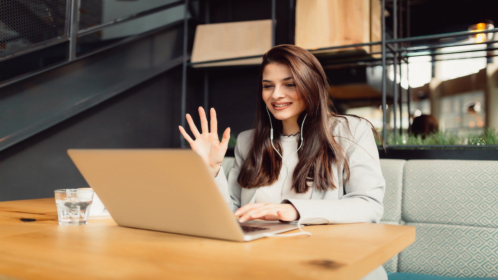 Beautiful young woman is having telephone conference skype call on her computer while sitting in cafe.