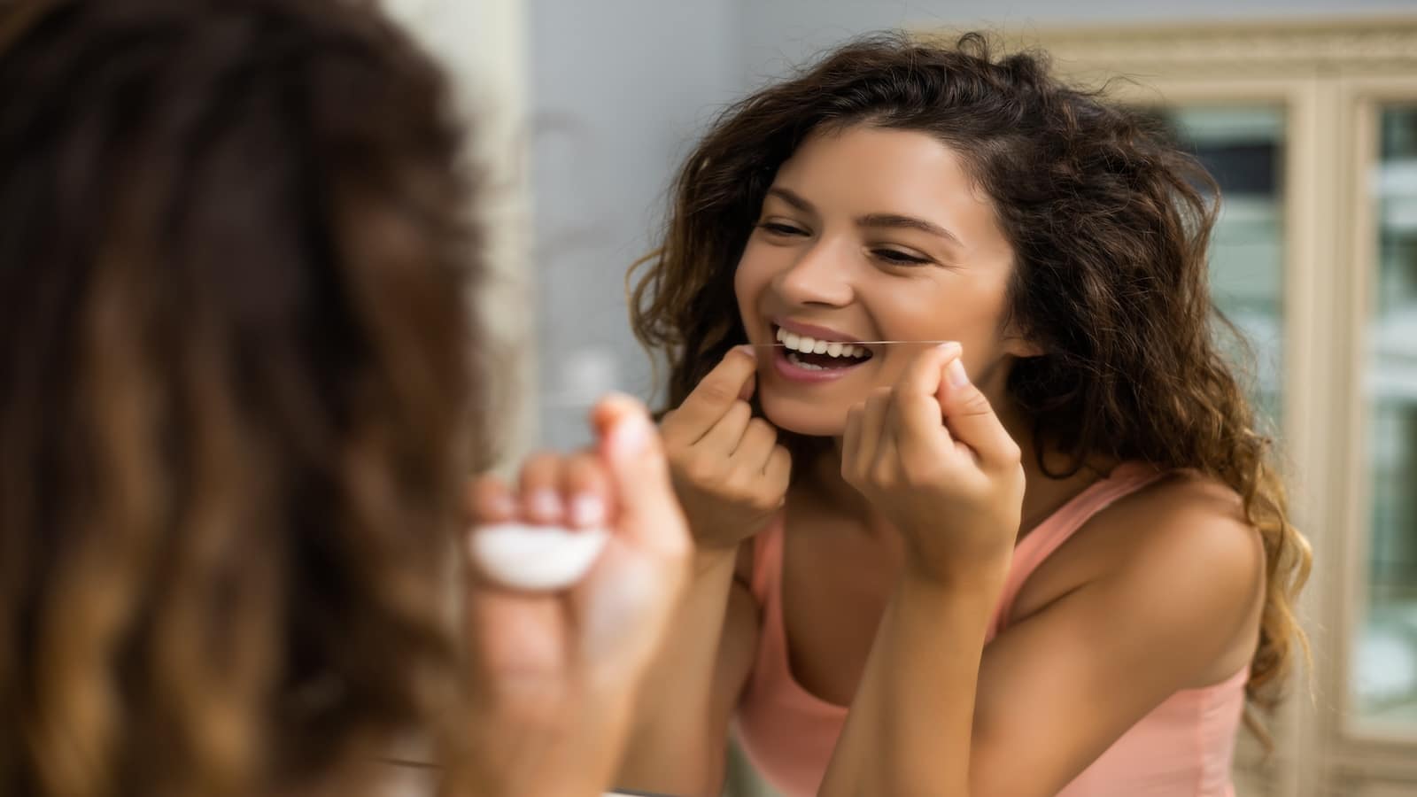 Woman using dental floss in the bathroom.