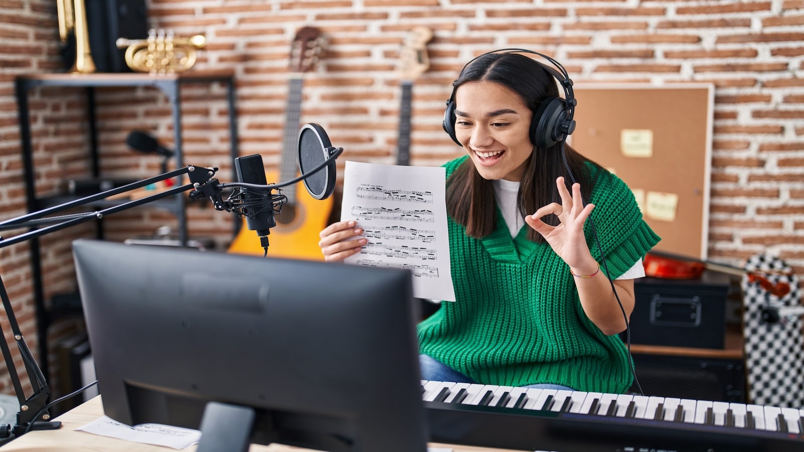 Young south asian woman doing online music tutorial showing music sheet doing ok sign with fingers, smiling friendly gesturing excellent symbol.