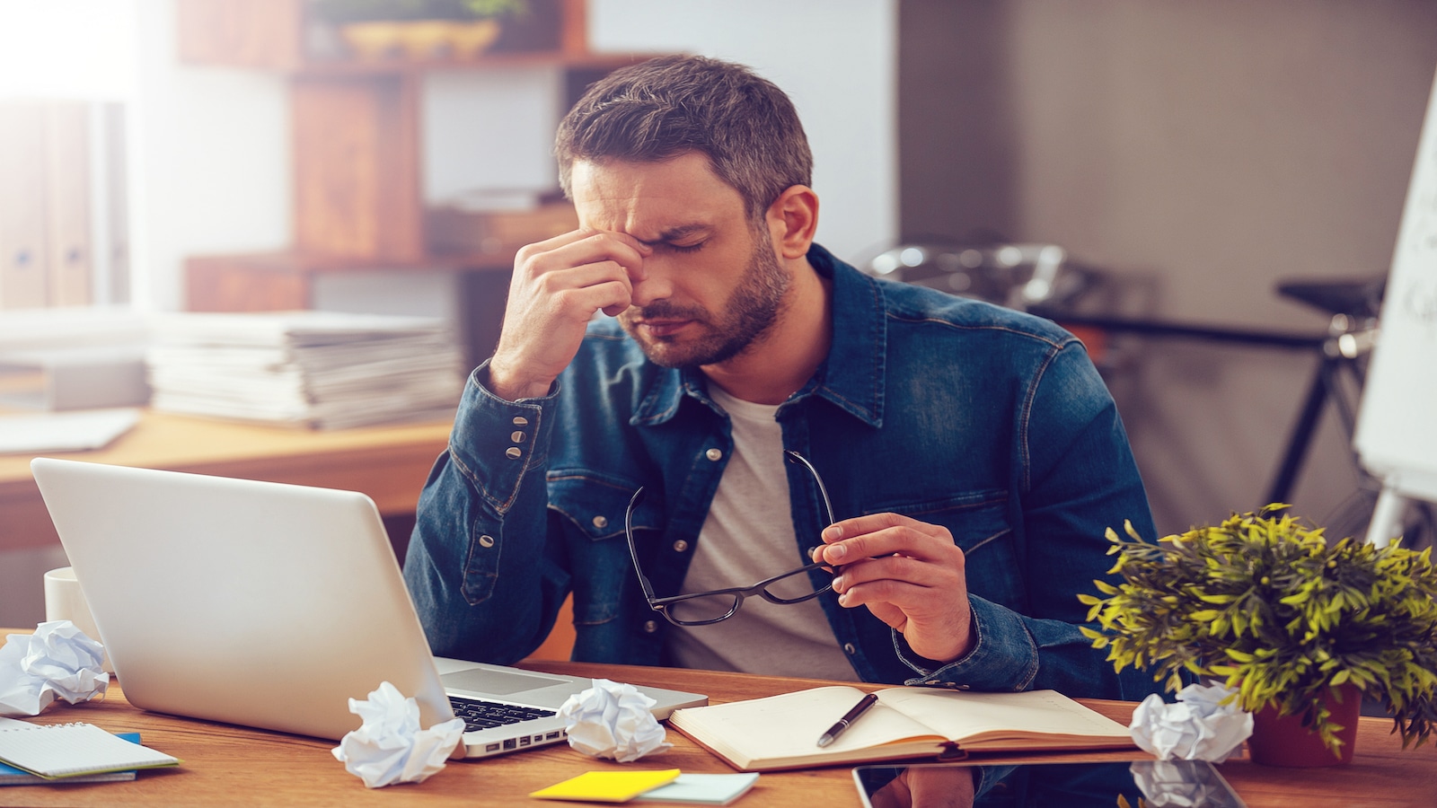 Frustrated young man massaging his nose and keeping eyes closed while sitting in office.