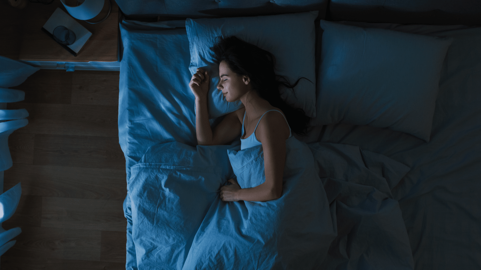 Top view of a young woman sleeping cozily on on a bed in a dark bedroom.