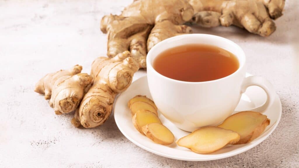 Cup of hot ginger tea with ginger root and slices on gray background.