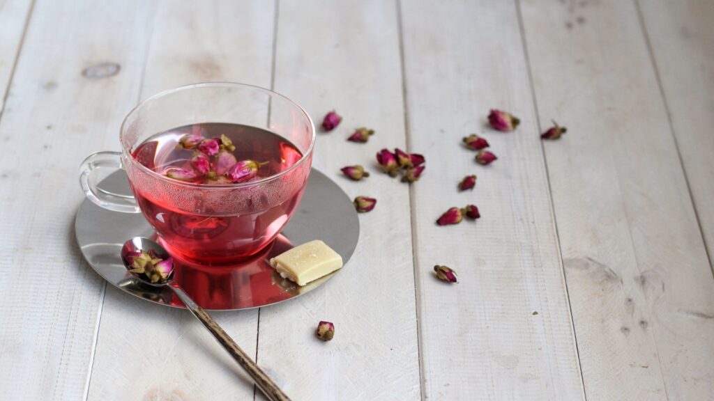Cup of rose tea in glass jar over white wooden surface.