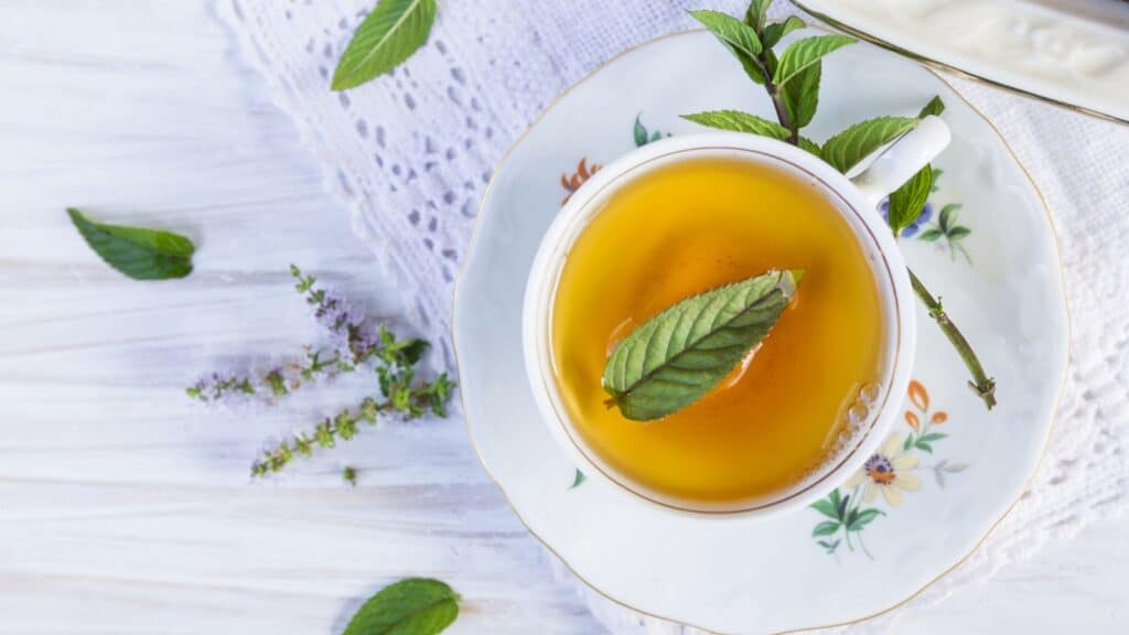 Cup of tea with peppermint on white wooden table with lacy napkin.