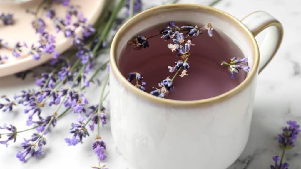 Fresh delicious tea with lavender and beautiful flowers on white marble table, closeup.