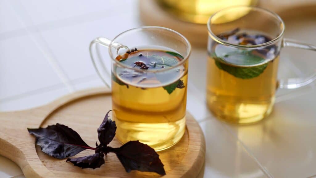 Tulsi or holy basil tea in transparent glass cup with fresh tulsi leaf white background. Ayurvedic medicine in India.