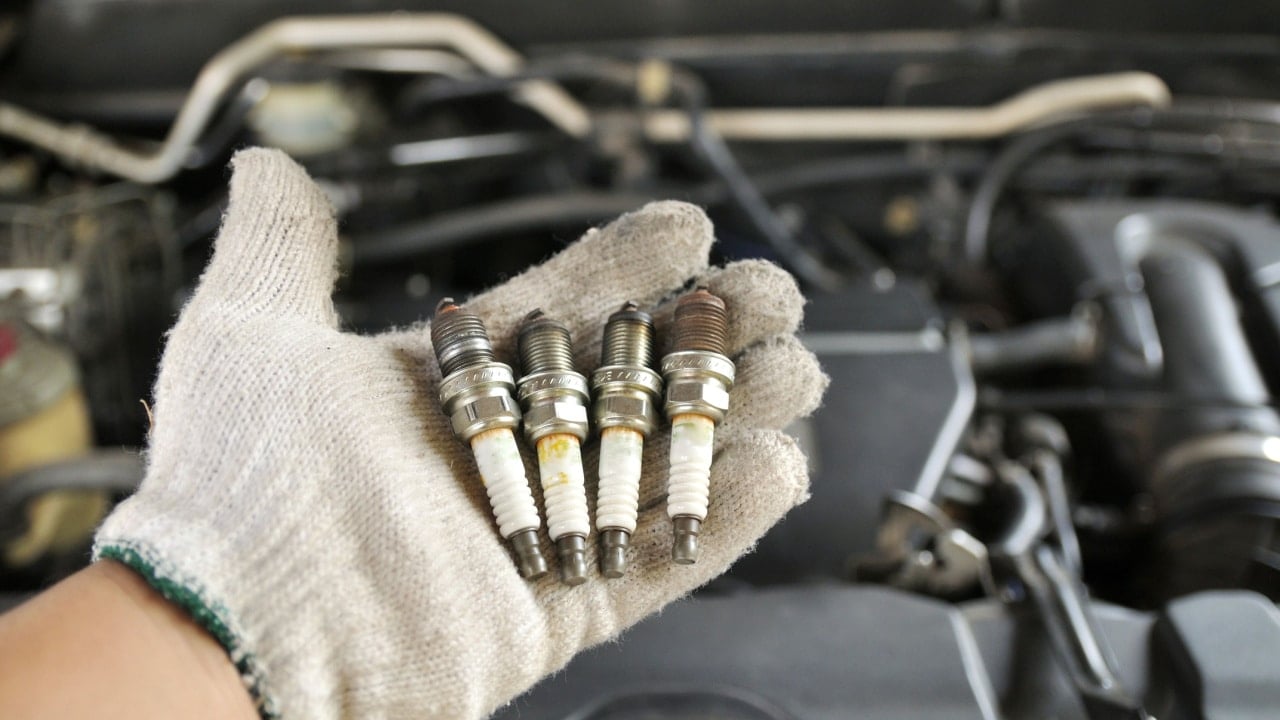 Stock Photo ID: 496502962. Dirty gloved hand carrying spark plugs for change to a new set by the maintenance team. Car spark plugs, spark plug insulators; hand holding car parts. Mechanic, maintenance, car workshop, auto shop, tune up.