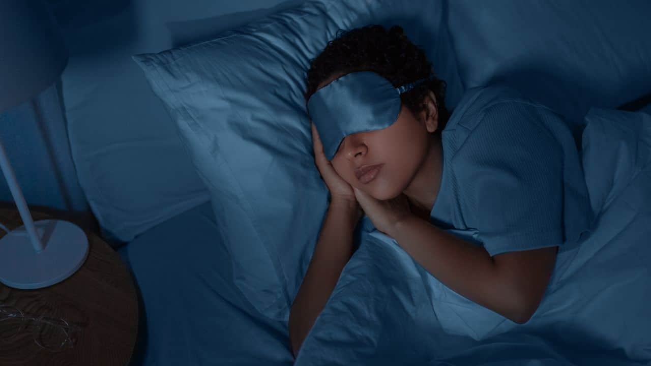 people, relax and comfort concept - young african american woman in eye mask sleeping in bed at home at night