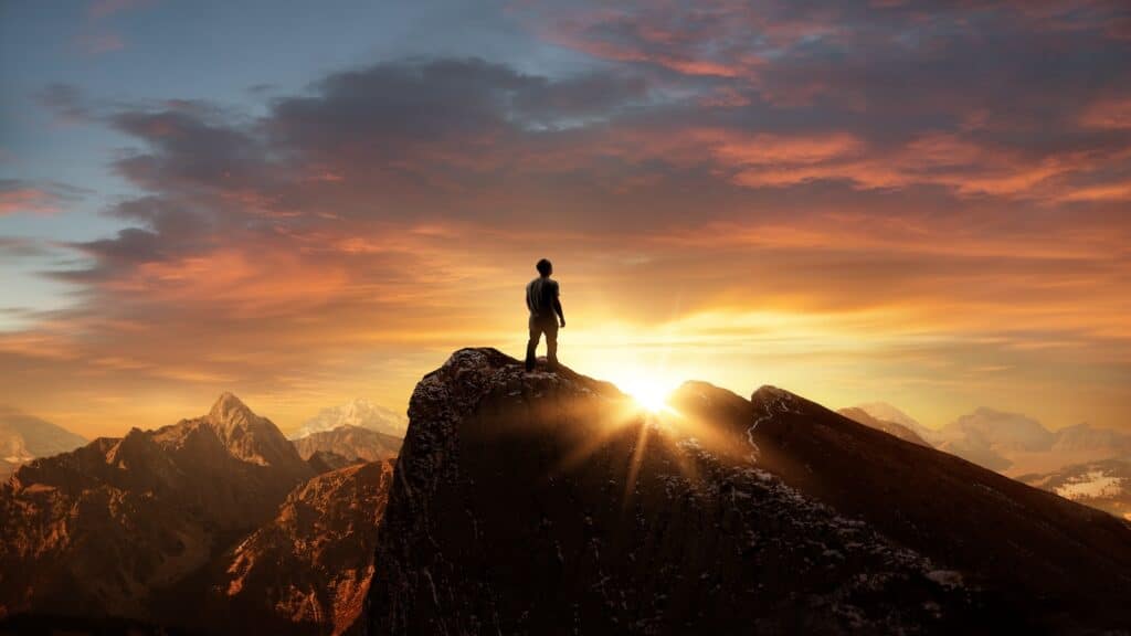 A man standing on top of a mountain as the sun sets.