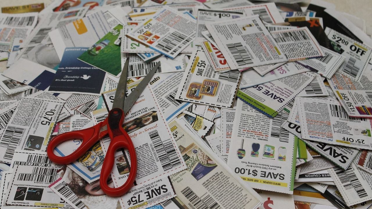 A large pile of coupons, topped with a pair of red scissors for clipping.