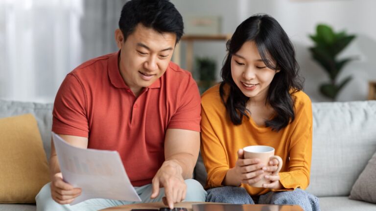 Happy asian family middle aged husband and young wife sitting on couch, holding documents