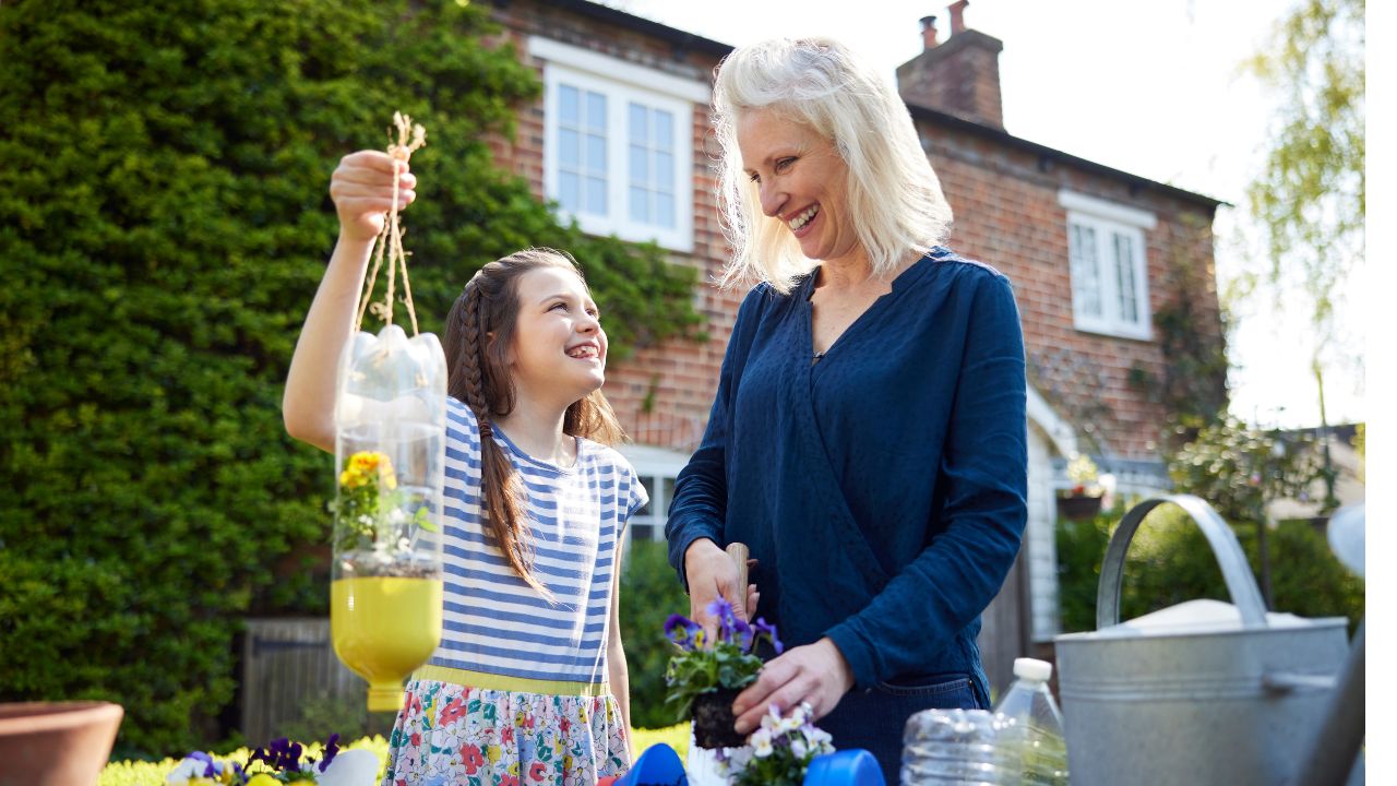 Mother And Daughter Making Recycled Plant Holders From Plastic Bottle Packaging Waste In Garden At Home