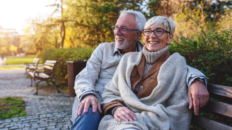 Smiling senior couple sitting on the bench in the park together enjoying retirement
