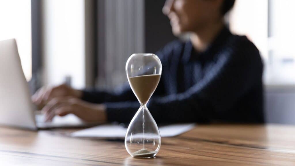 Close up hourglass measuring time, businesswoman working on computer.