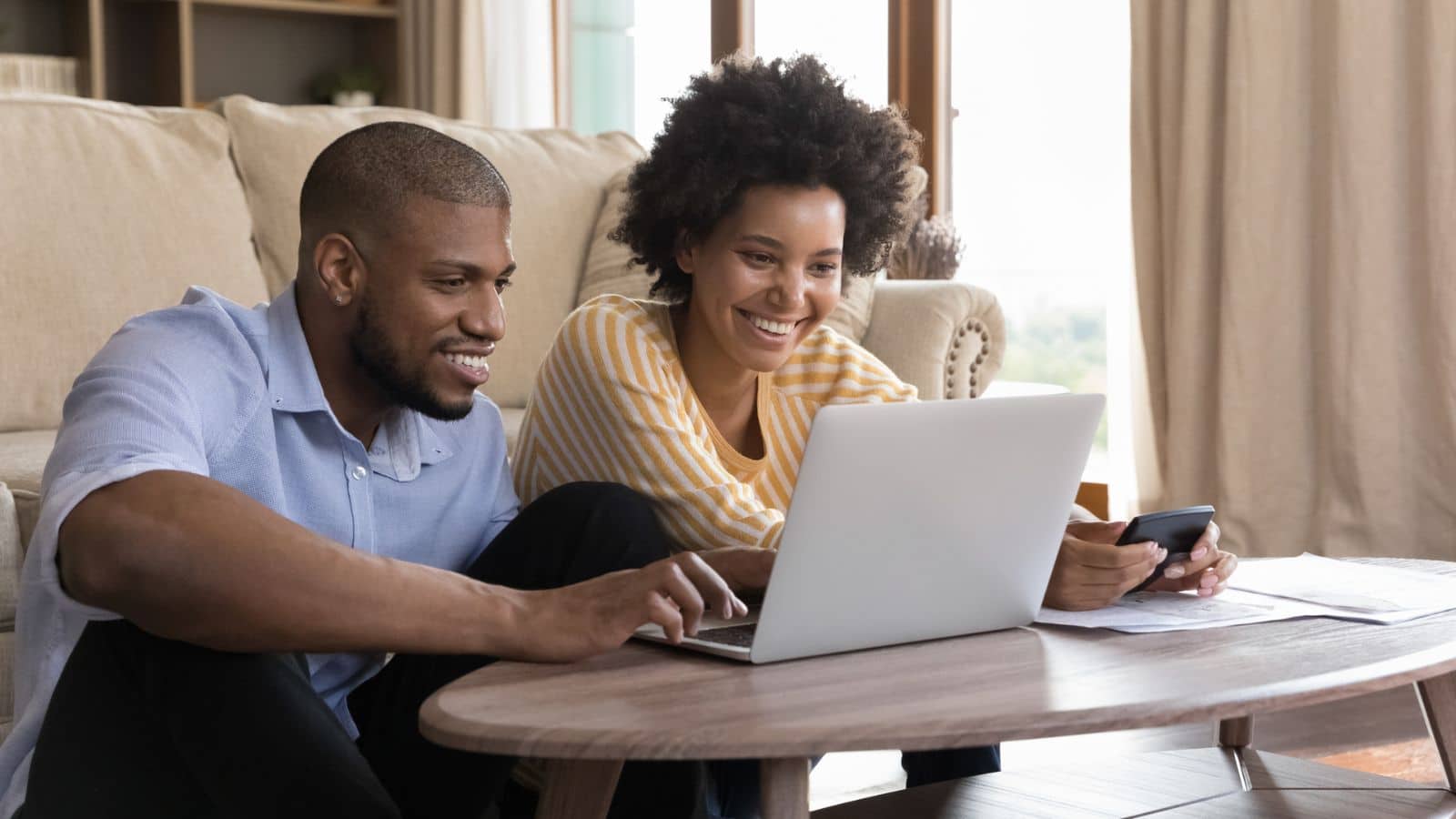 Happy young couple using laptop, looking at screen, smiling working on budget