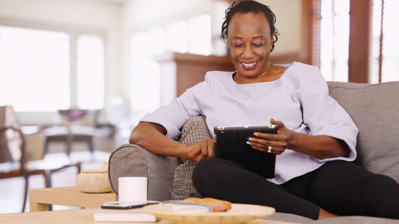 An older woman uses her tablet while relaxing on the couch.