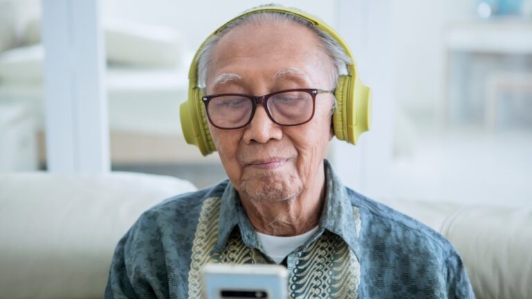Elderly man wearing headphones listening on cell phone