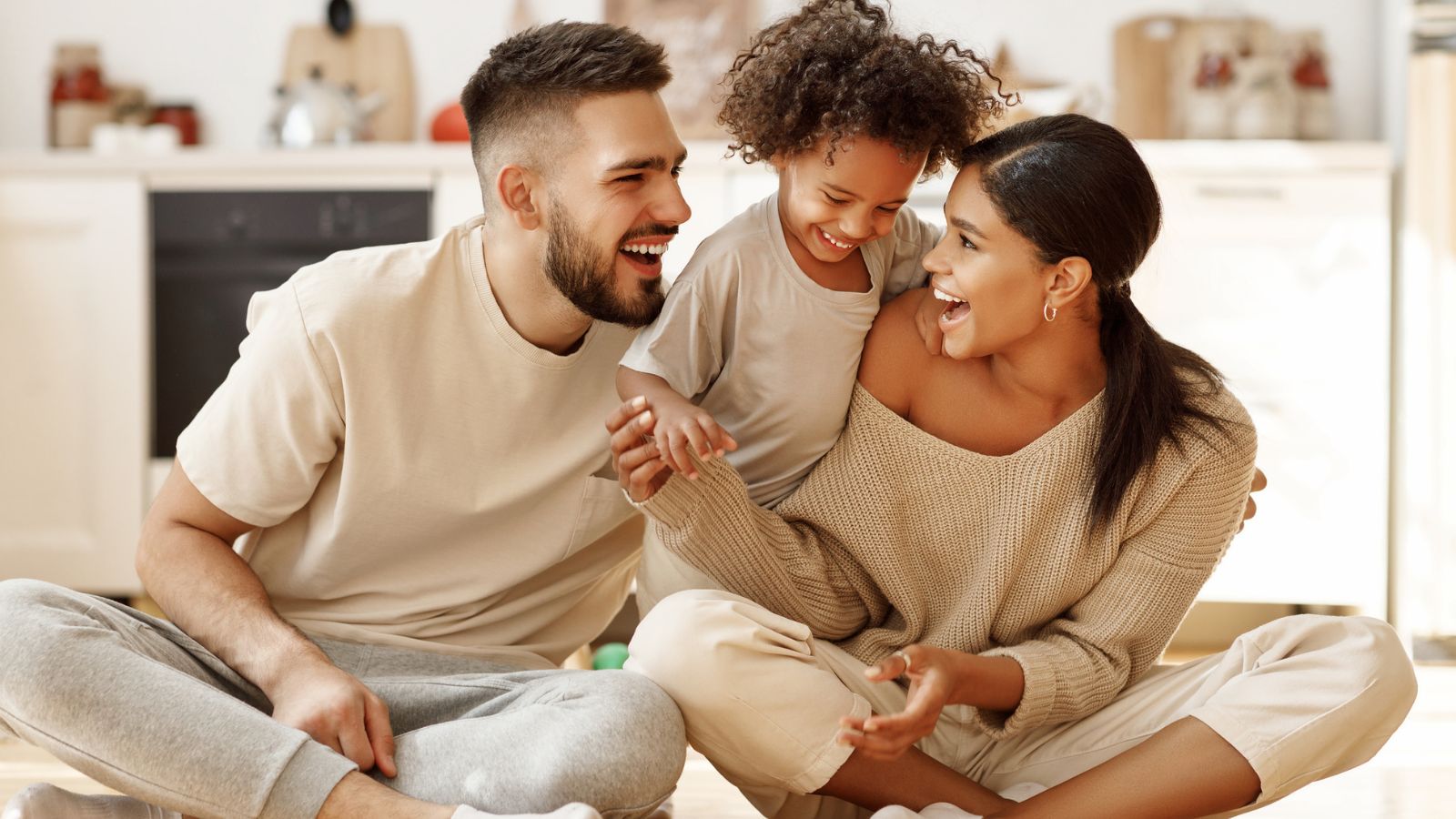 Happy family mom, dad and child laughing, playing and tickles on floor in cozy kitchen at home.