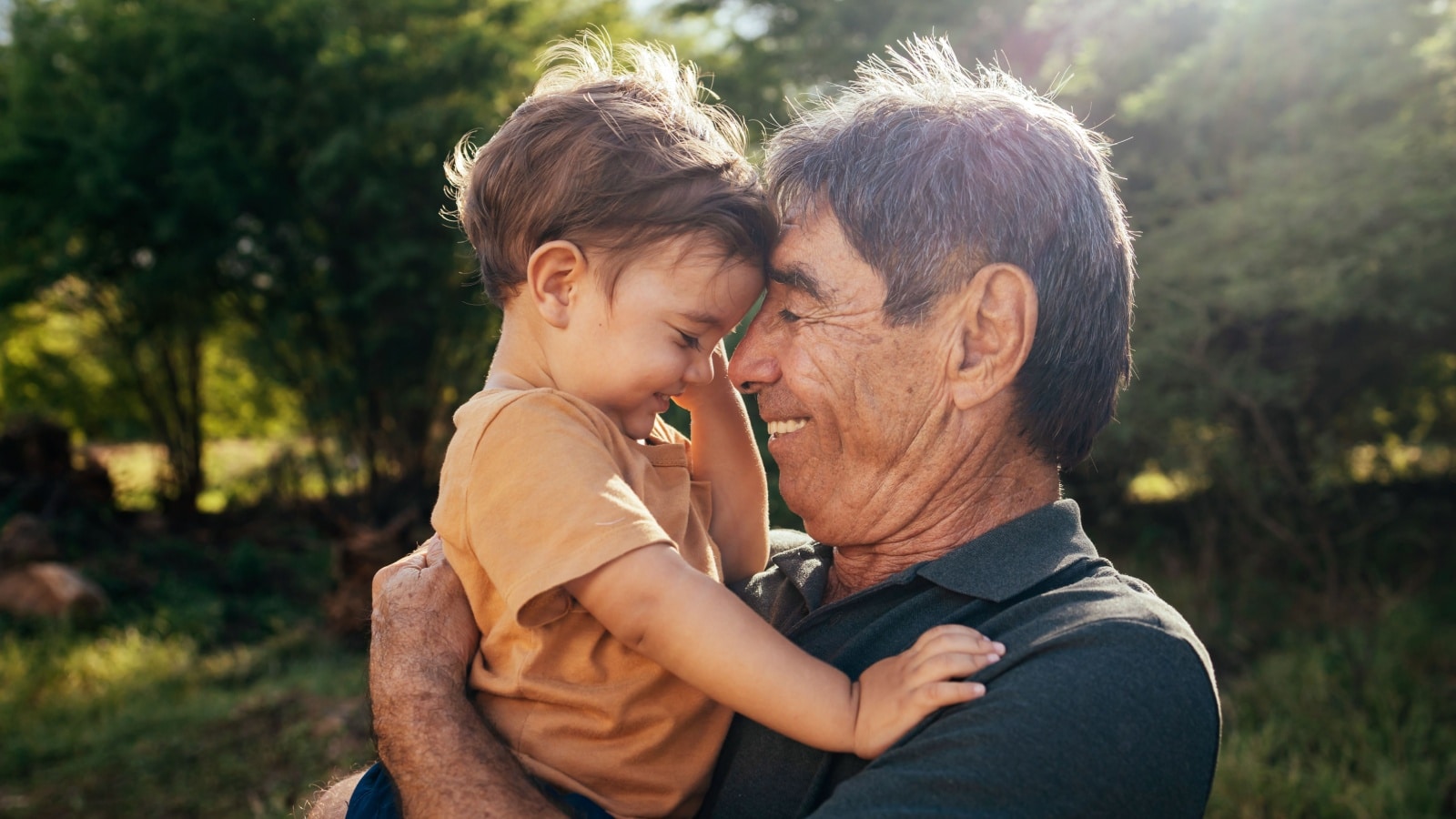 Playful grandfather spending time with his grandson in park on sunny day.