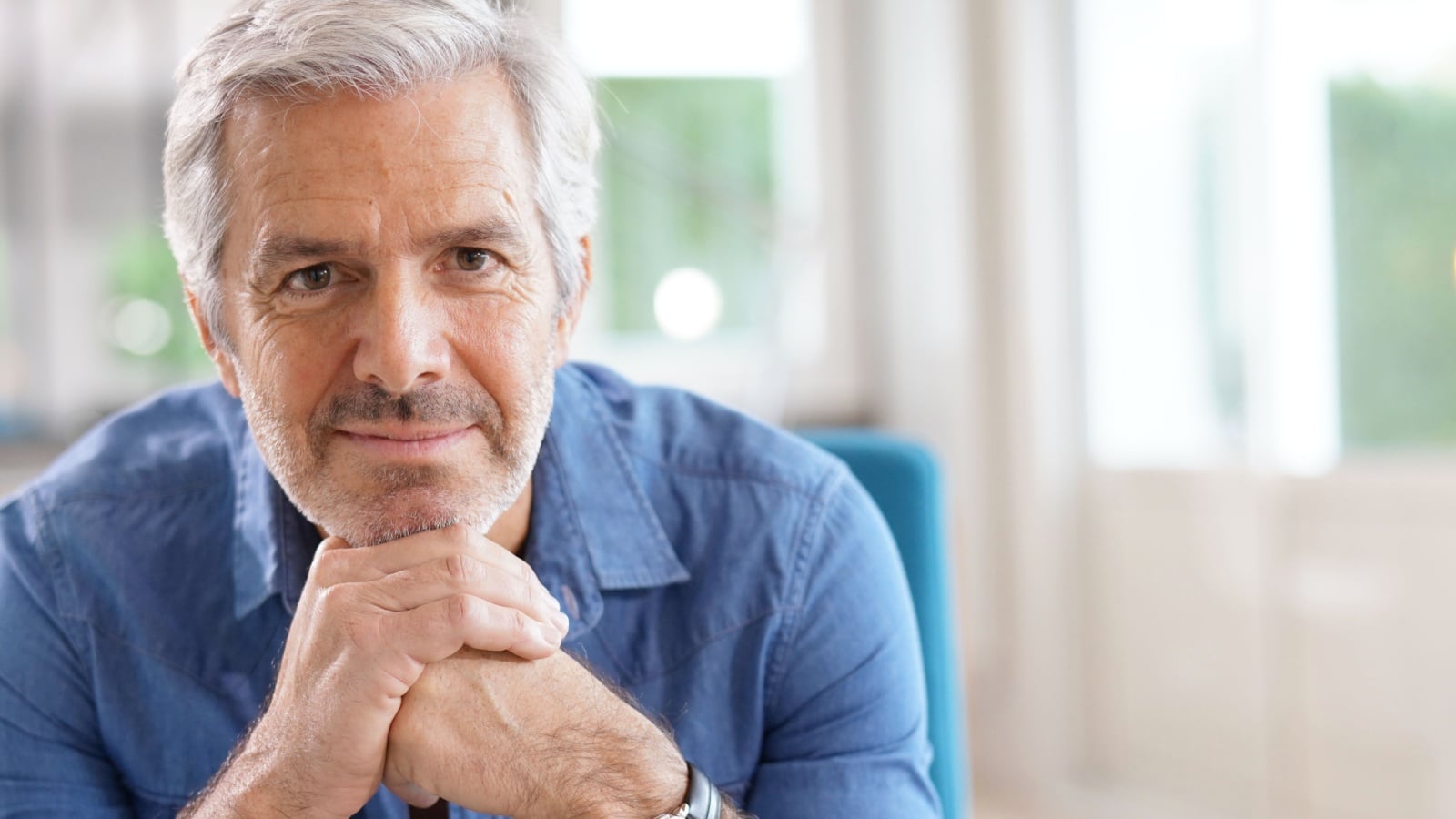 Older man with grey hair and blue shirt looking at camera.