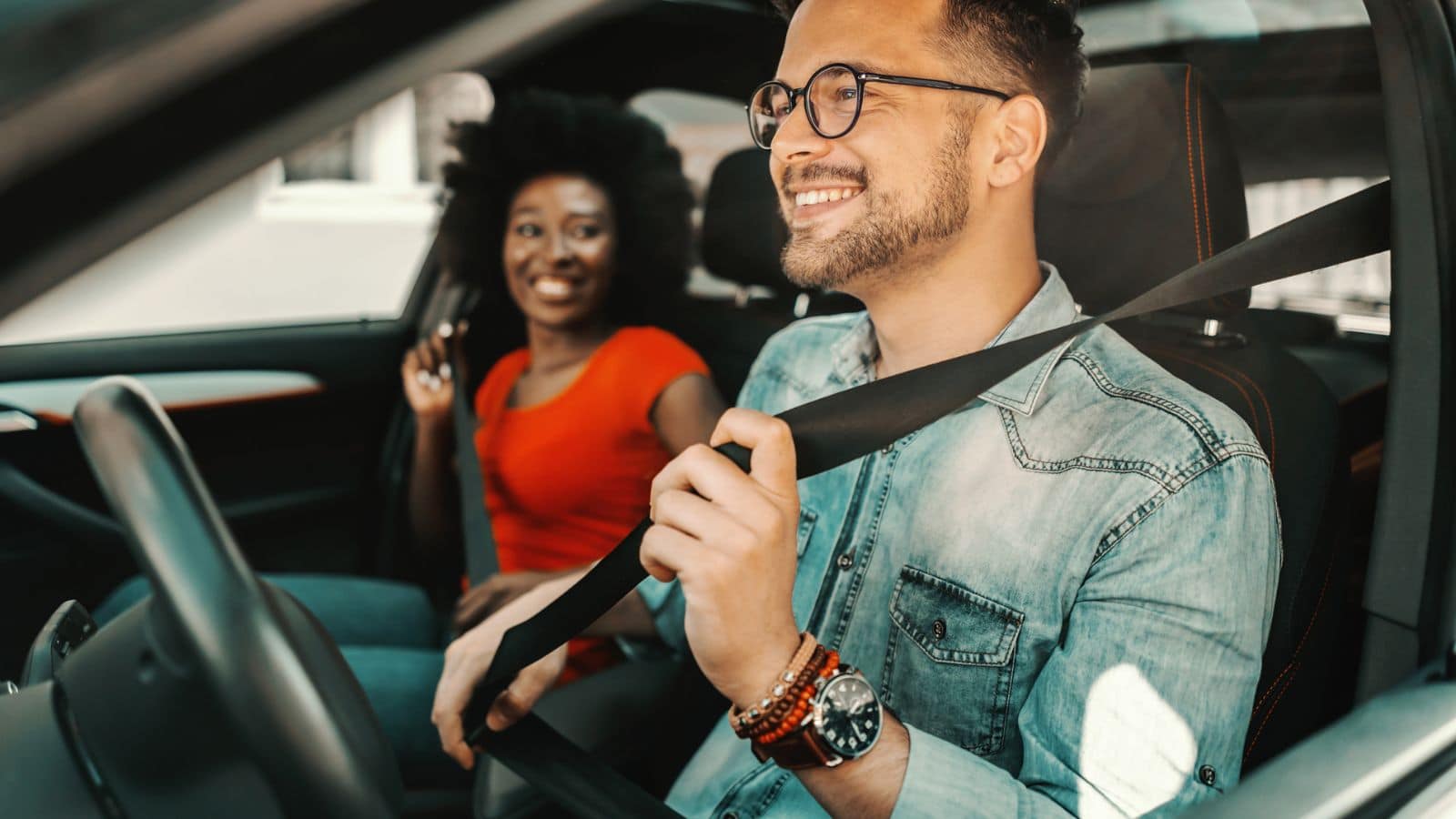 Young couple sitting in a car and fastening seat belts