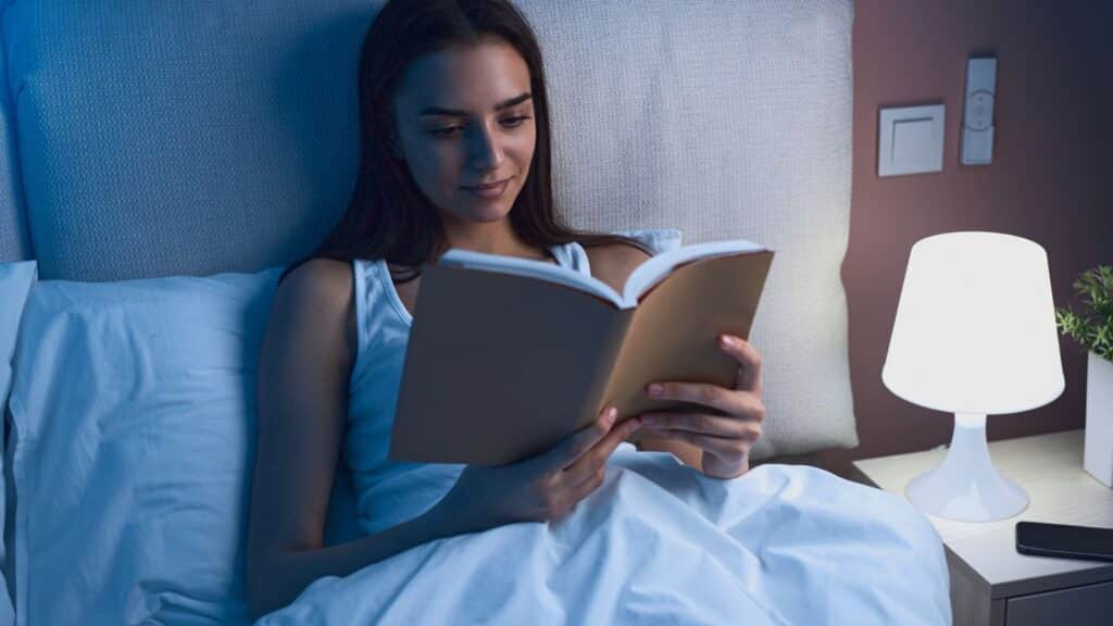 Young woman reading book in bed at night.