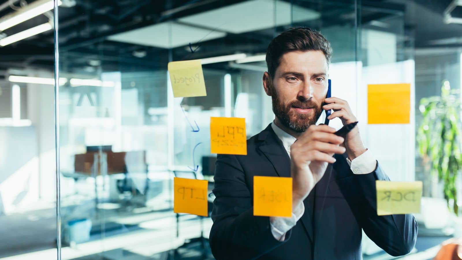business man hanging reminders on sticky notes on glass board.