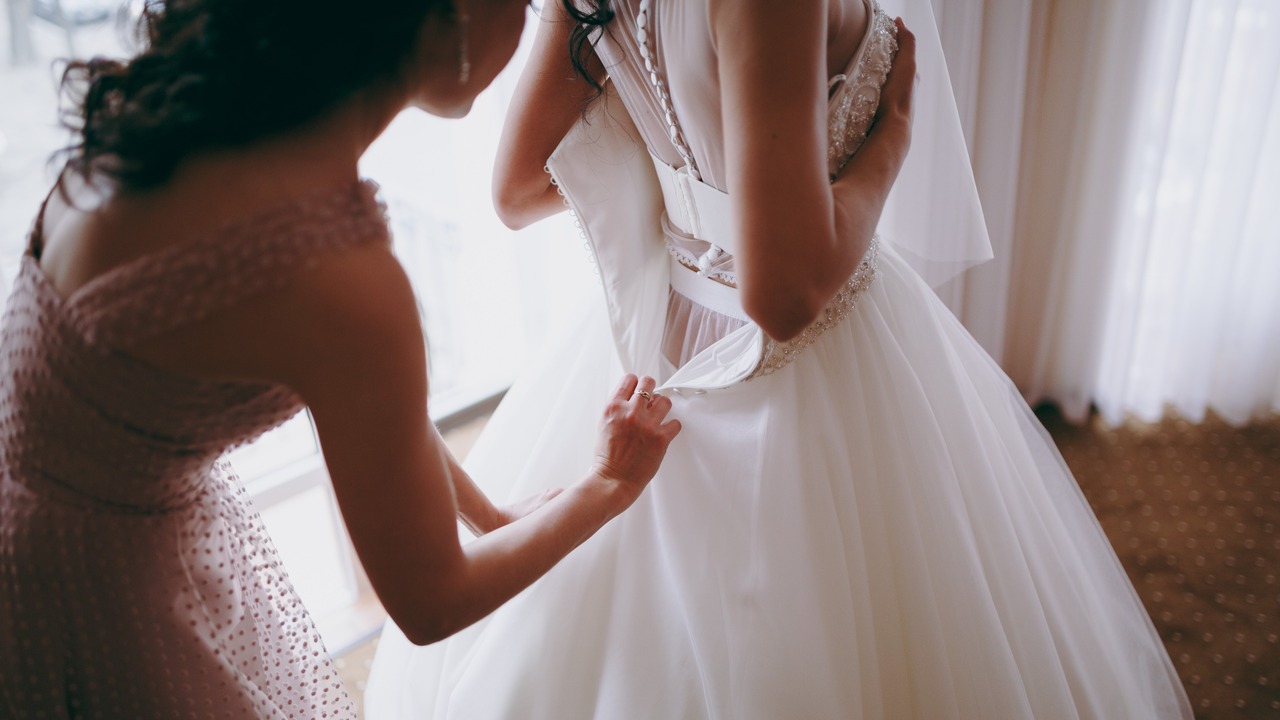 Bridesmaid helping bride lacing her wedding white dress. 664761526