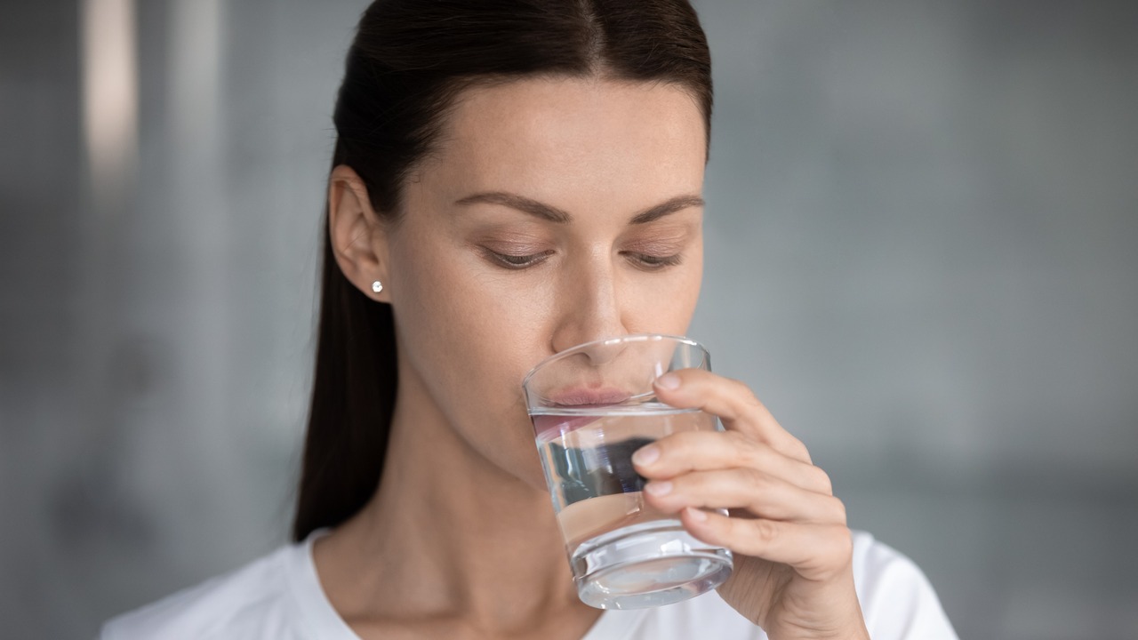 A young woman drinking water from a glass cup.