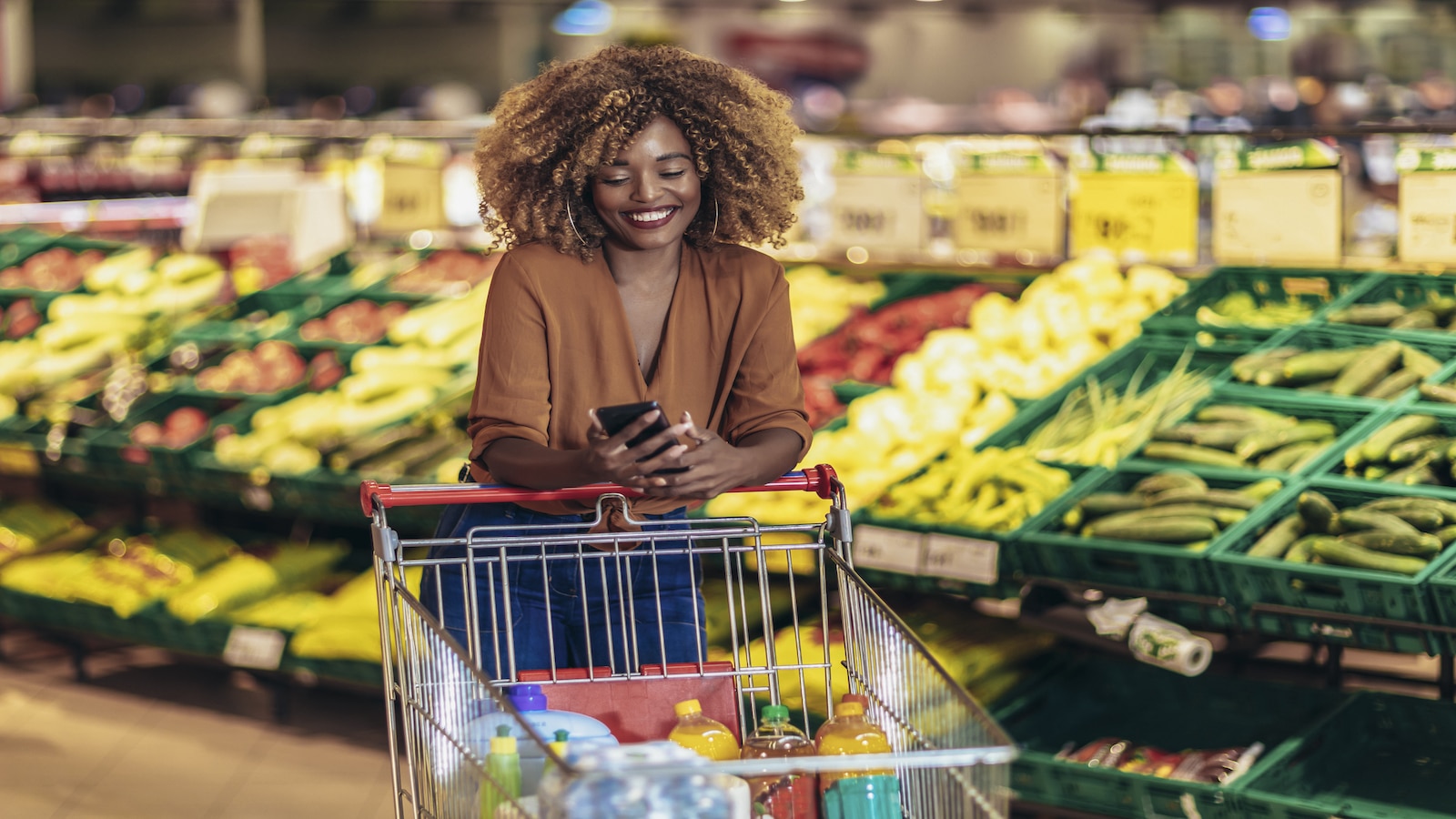 Cheerful woman shopping in grocery store vegetable section.