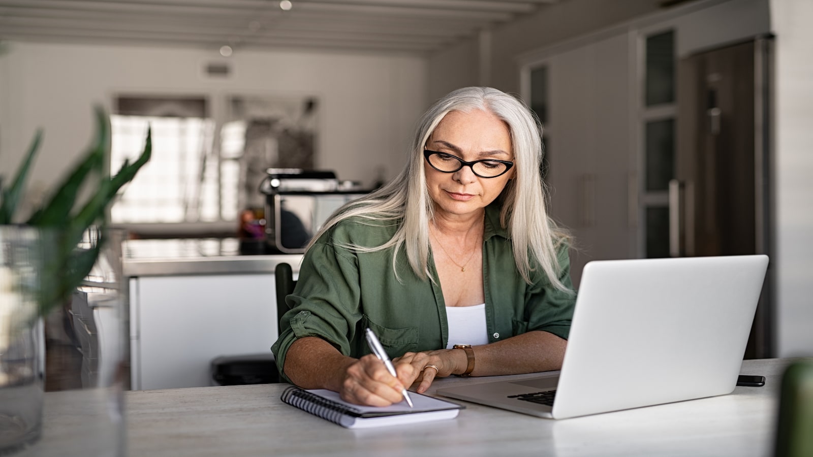 serious woman writing in notebook paying bills at computer.