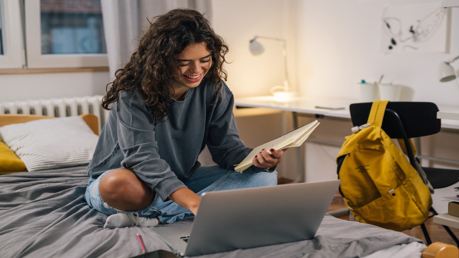 young girl sitting on bed working on computer.