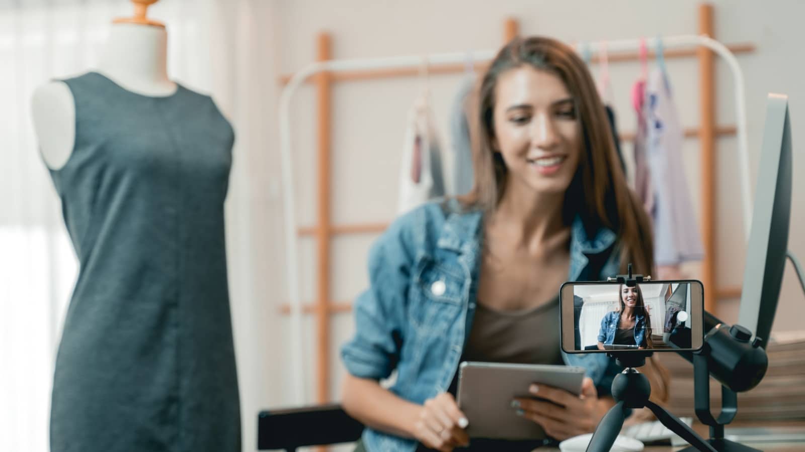 Beautiful asian woman blogger showing clothes in front of camera to recording vlog video live streaming at her shop.Business online influencer on social media concept.
