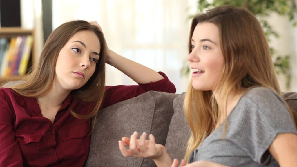 Bored girl listening to her friend having a conversation sitting on a couch in the living room at home.
