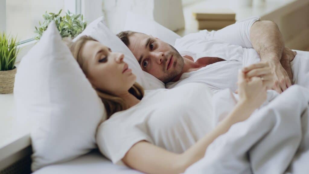 Closeup of couple with relationship problems having emotional conversation while lying in bed at home.