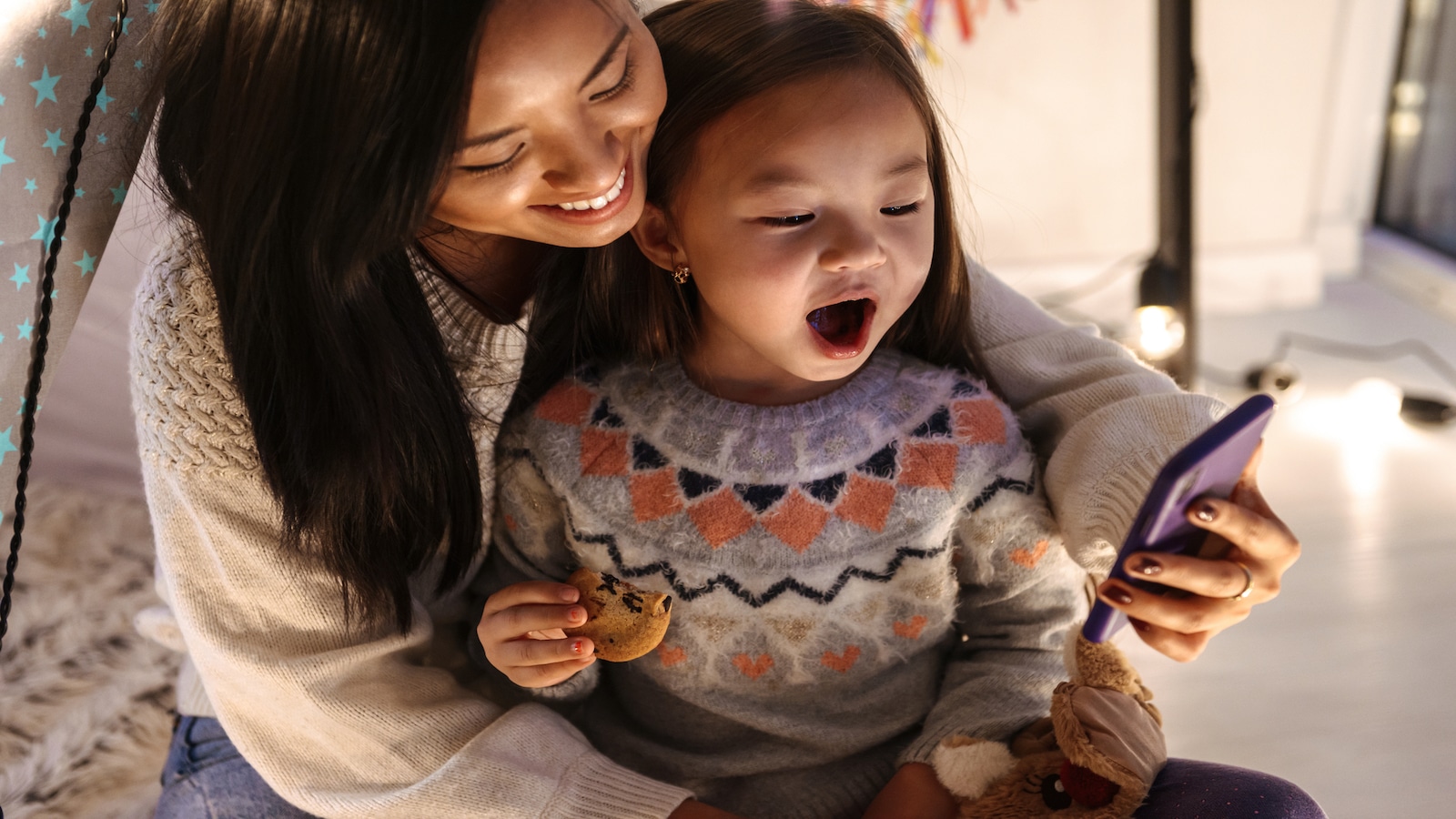 Happy young woman with her little daughter girl having fun on floor using mobile phone Christmas time.