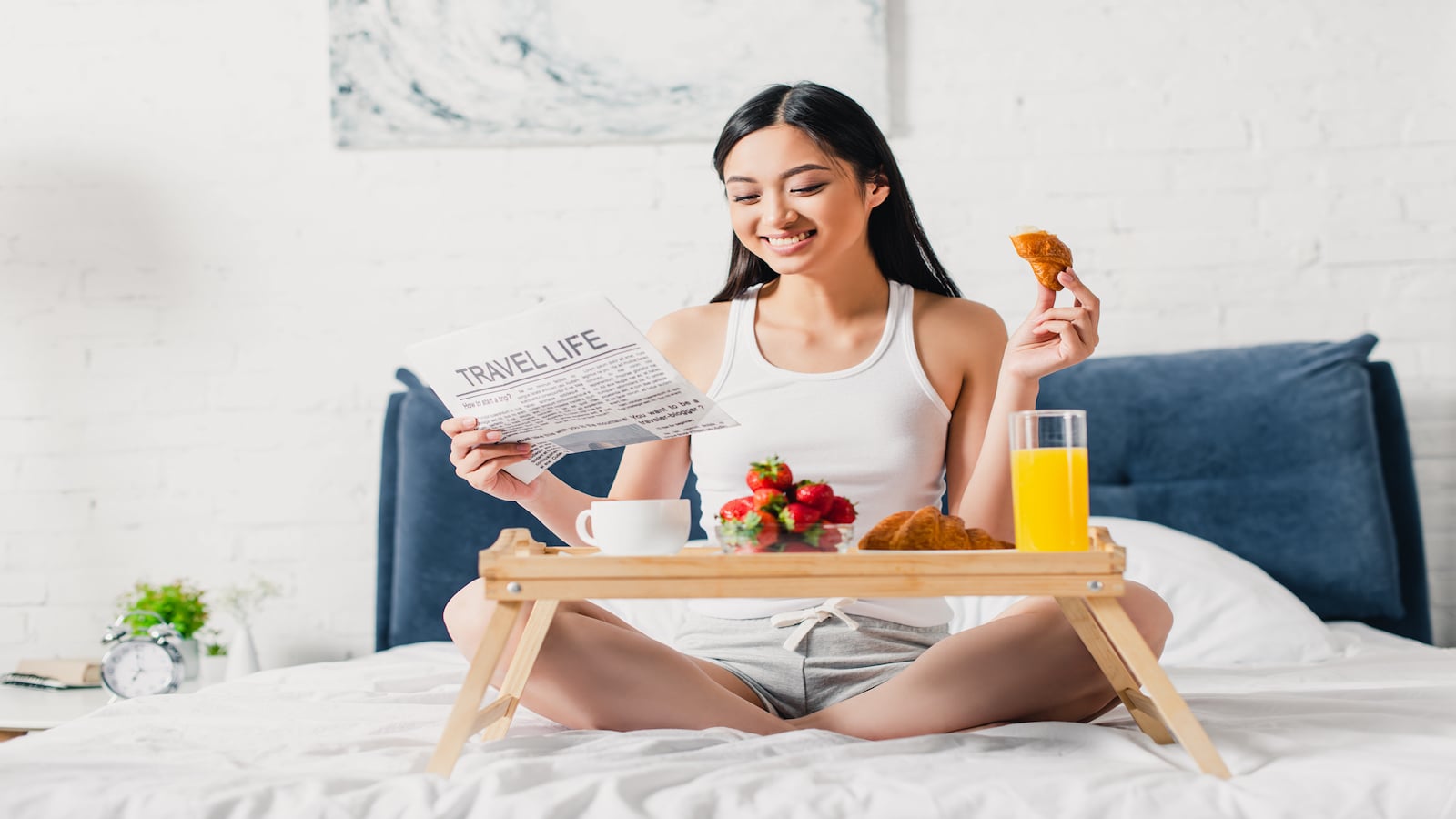 Woman smiling eating breakfast in bed.