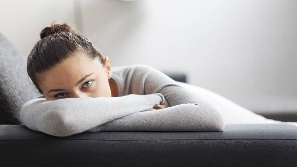 Stressed unhappy sad young woman laying down on couch.