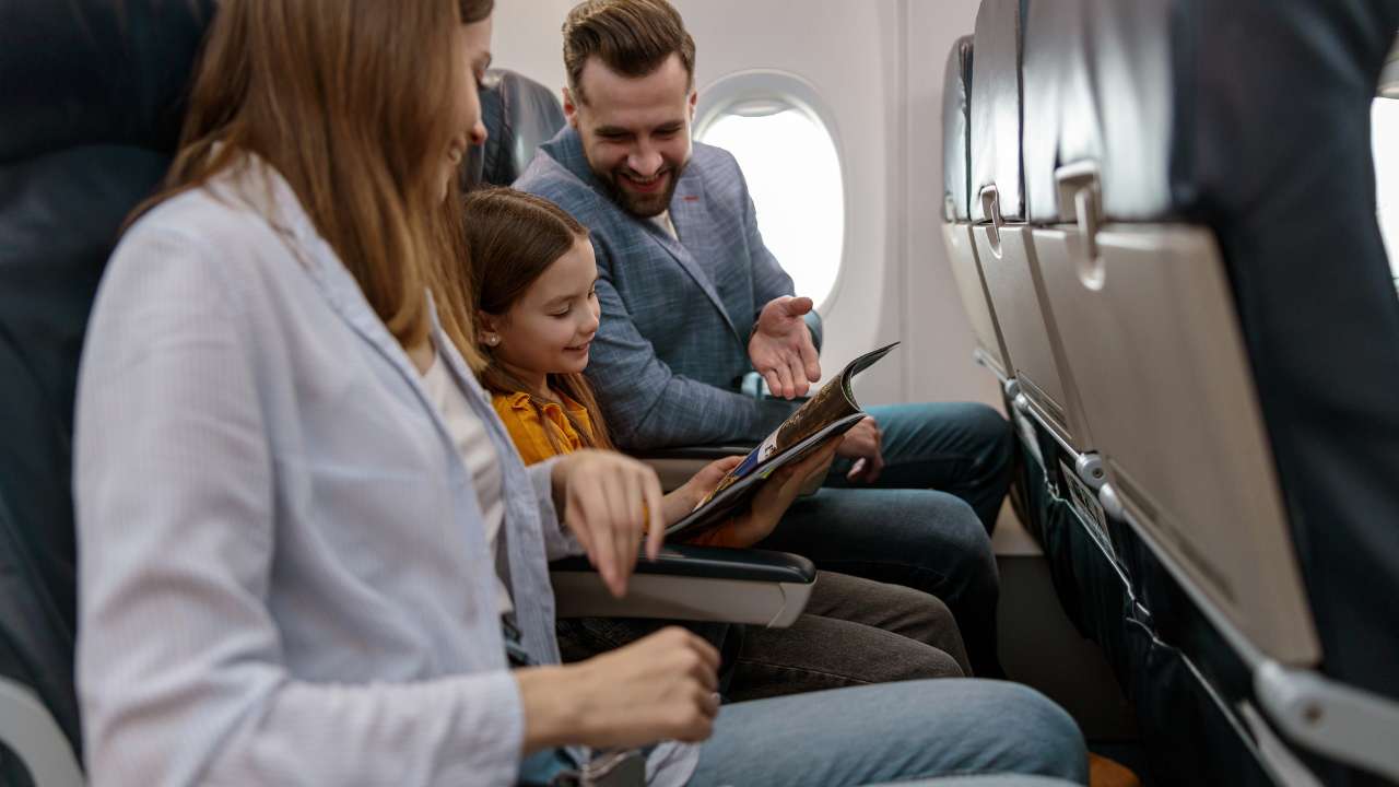 Dad, mom, and young girl seated on plane smile while reading magazine.
