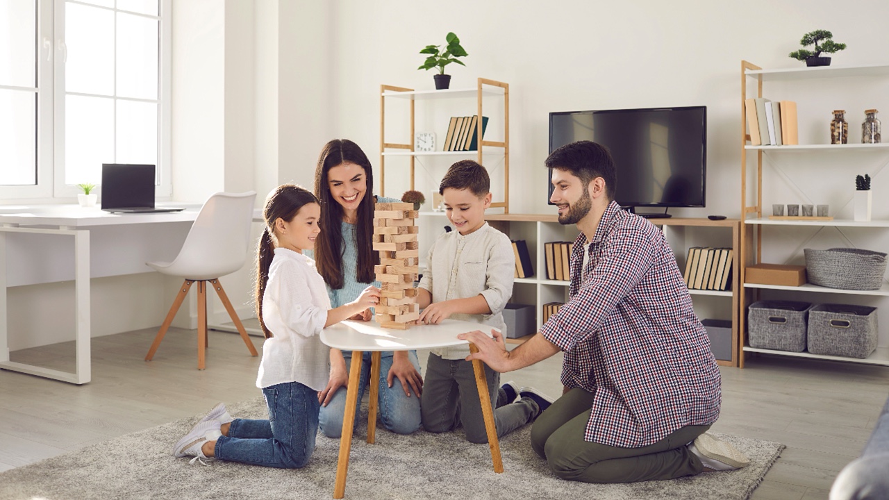Happy family with kids playing board games at home. Smiling mom, dad and children sitting on the floor around a low table in a cozy living room and pulling wooden blocks from the tower, living room