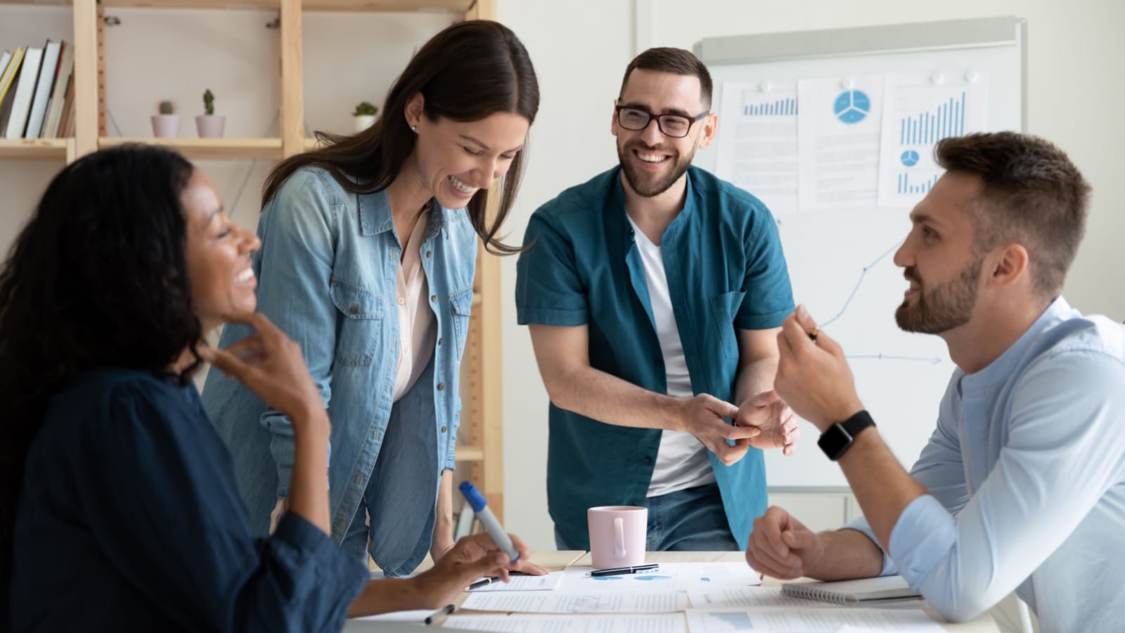 Smiling diverse colleagues gather in boardroom brainstorm.