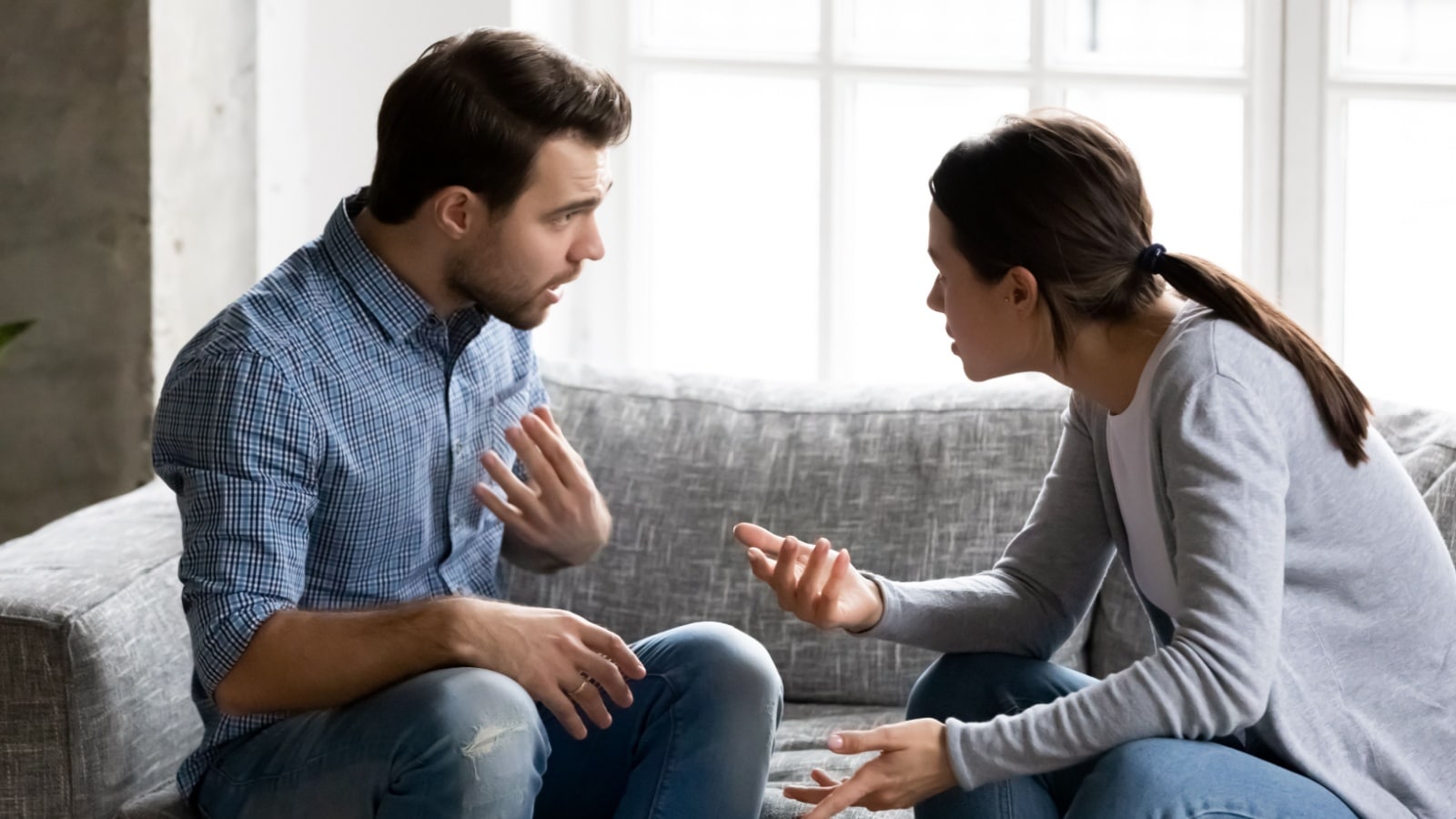 Stressed young married family couple arguing emotionally, blaming lecturing each other, sitting on couch. Depressed husband quarreling with wife, having serious relations communication problems.