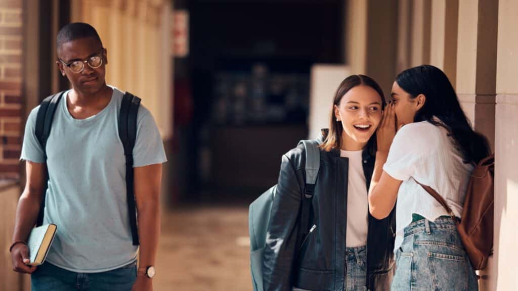 Students, bullying and whisper to gossip in school about sad boy, racism victim and social outcast. Girls gossiping about depressed, lonely and young teenager with anxiety, depression and rejection.