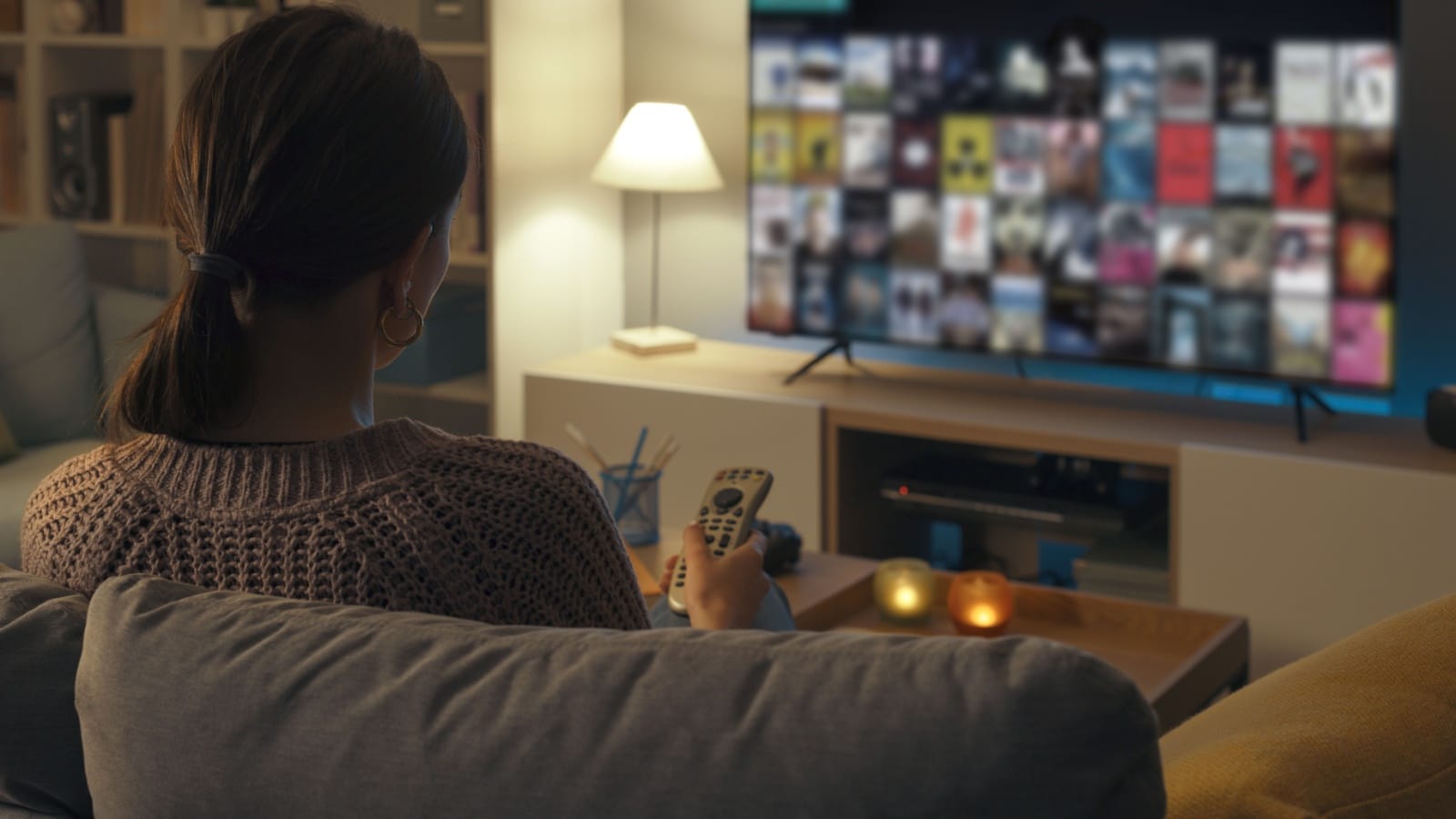 Woman relaxing on the couch, she is using the remote control and choosing a TV show or movie on the television menu.