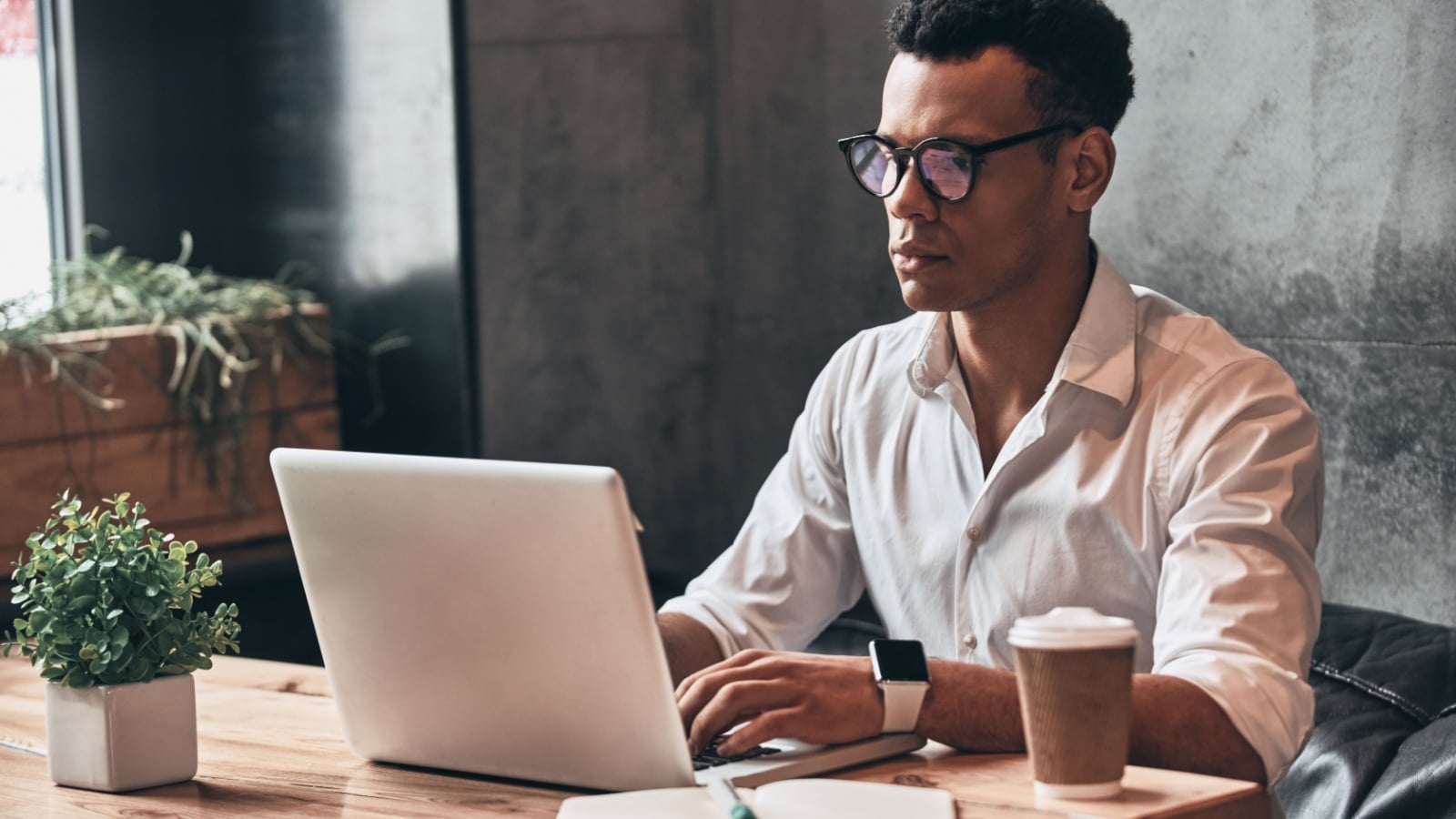 Young perfectionist. Handsome young African man in eyewear working using laptop while sitting in the office.