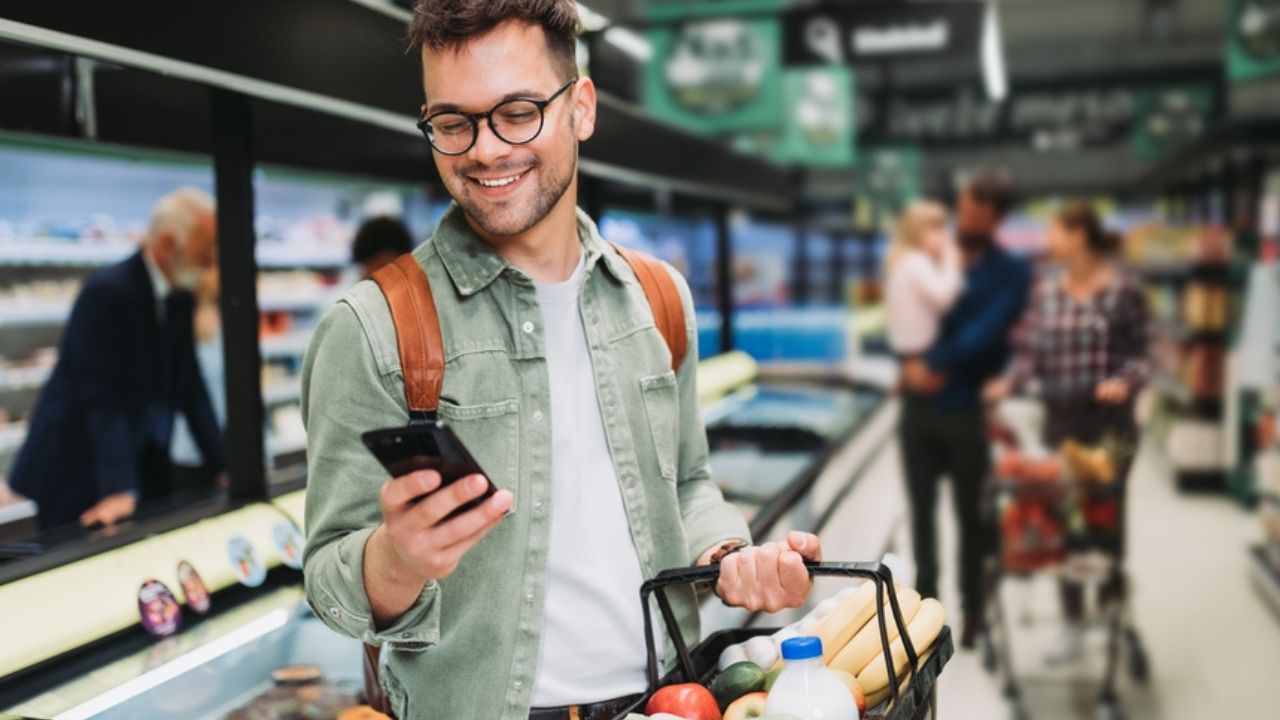 Young man buying groceries at the supermarket. Other customers in background. Consumerism concept.