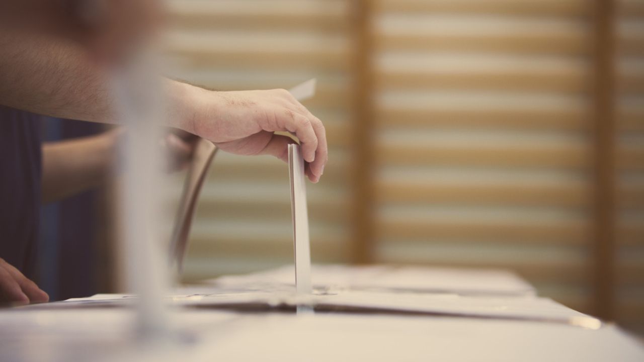 Hand of a person casting a ballot at a polling station during voting.