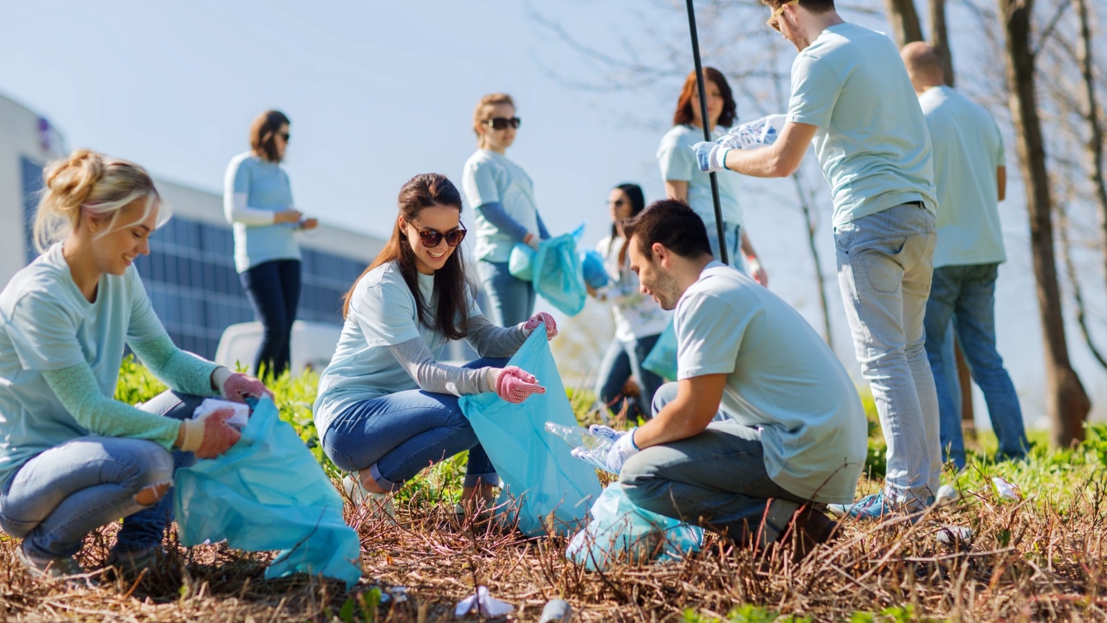 Group of happy volunteers with garbage bags cleaning area in park.