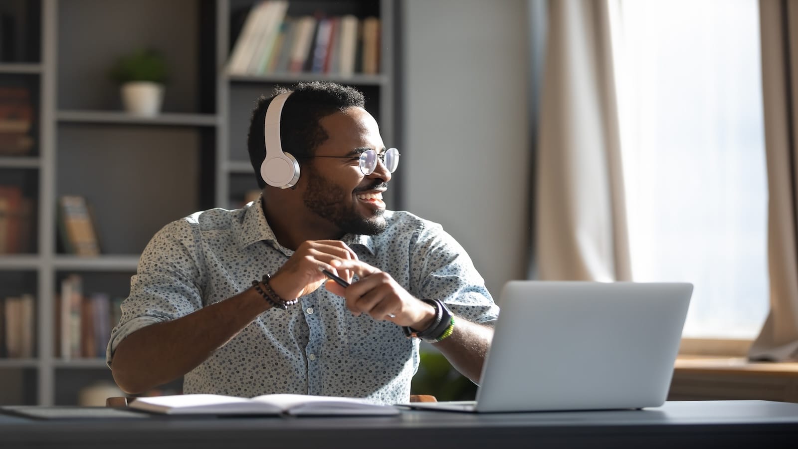 Happy relaxed man wearing wireless headphones look away rest at workplace finished work listening music podcast feel peace of mind.